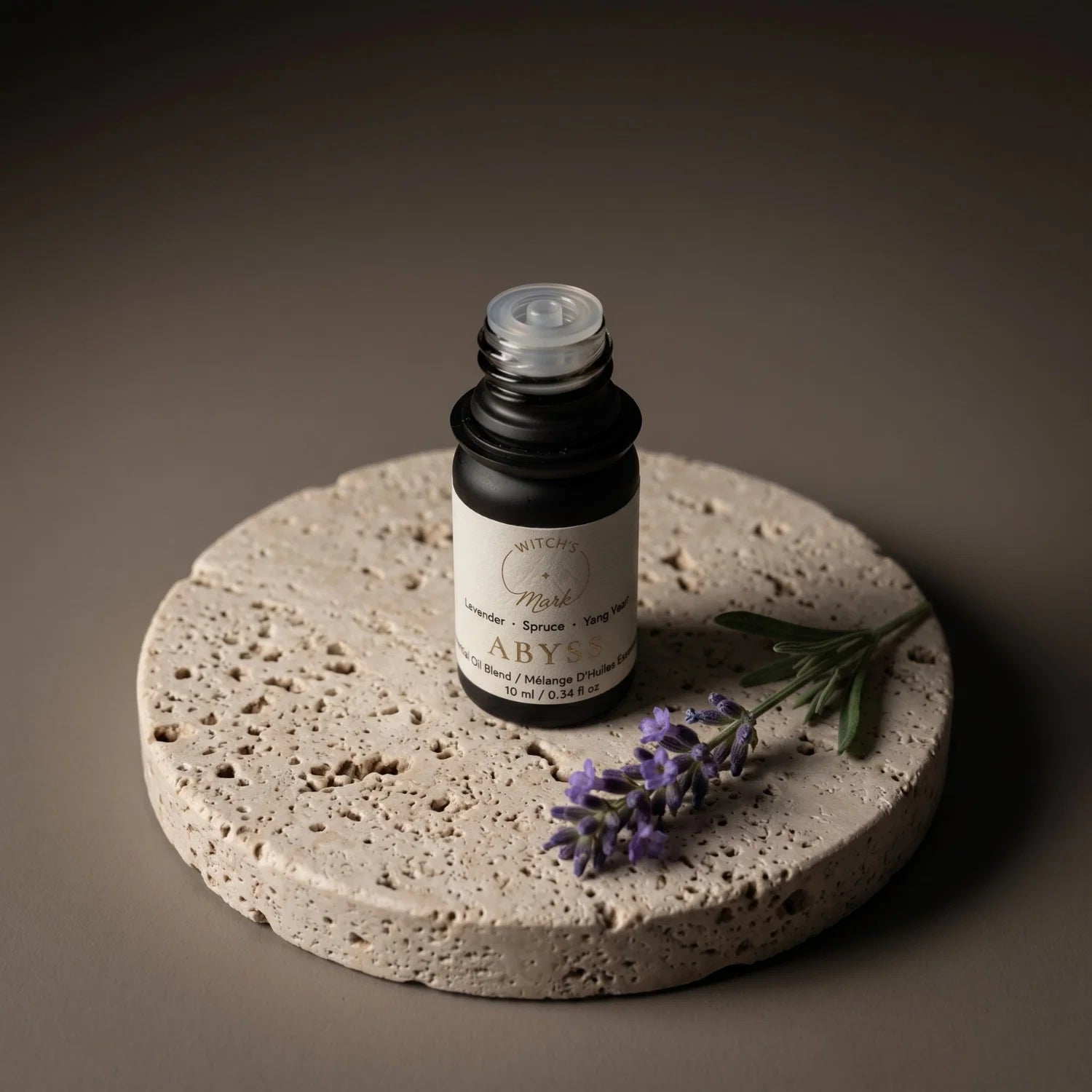 Abyss essential oil bottle next to a sprig of lavender on a porous stone coaster.