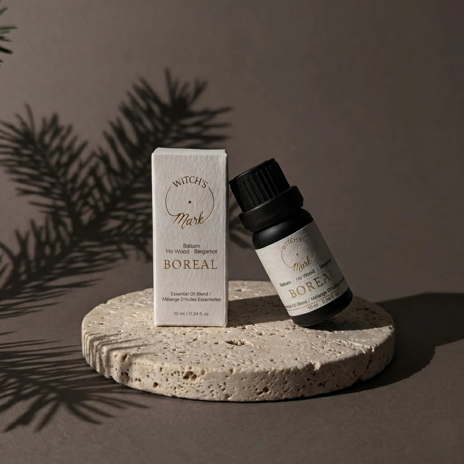 Boreal essential oil blend bottle with box packaging on a porous stone coaster. In the background there is a shadow of a balsam branch.