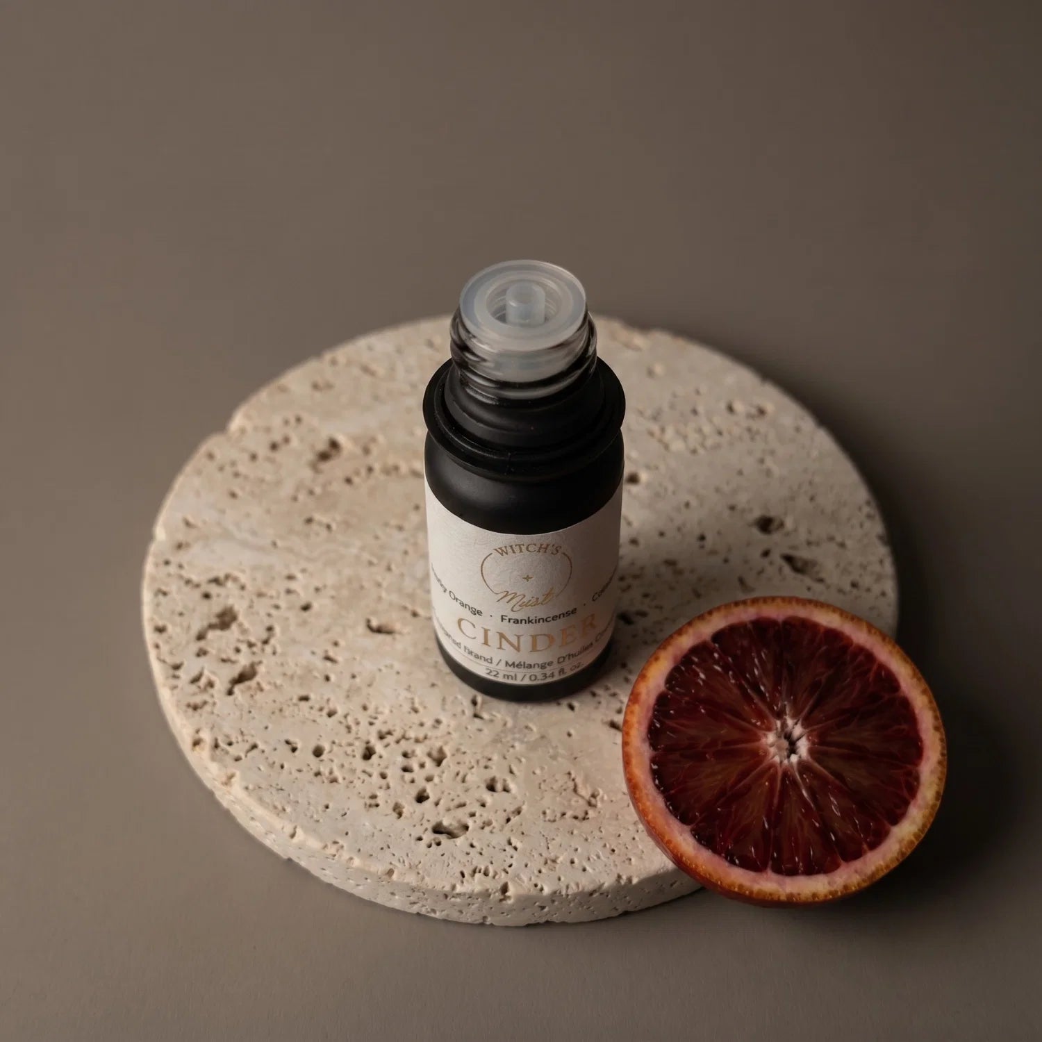 Bottle of essential oil labeled 'Cinder' on a stone surface with a sliced blood orange.