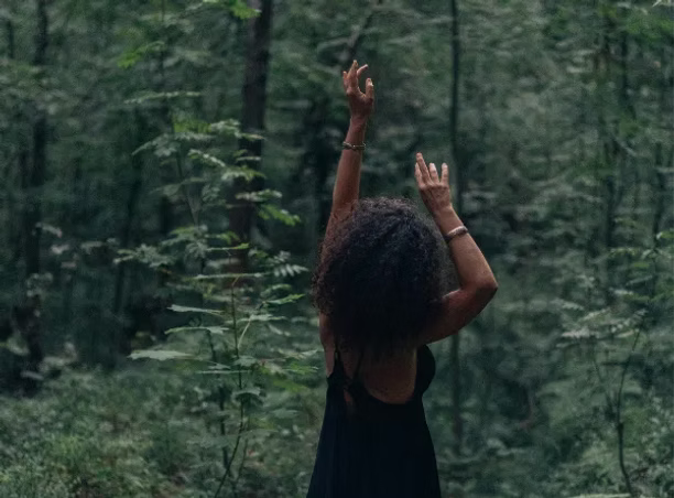 Witch with arms raised in a forest