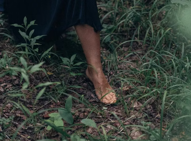 Witch walking barefoot on grass and leaves