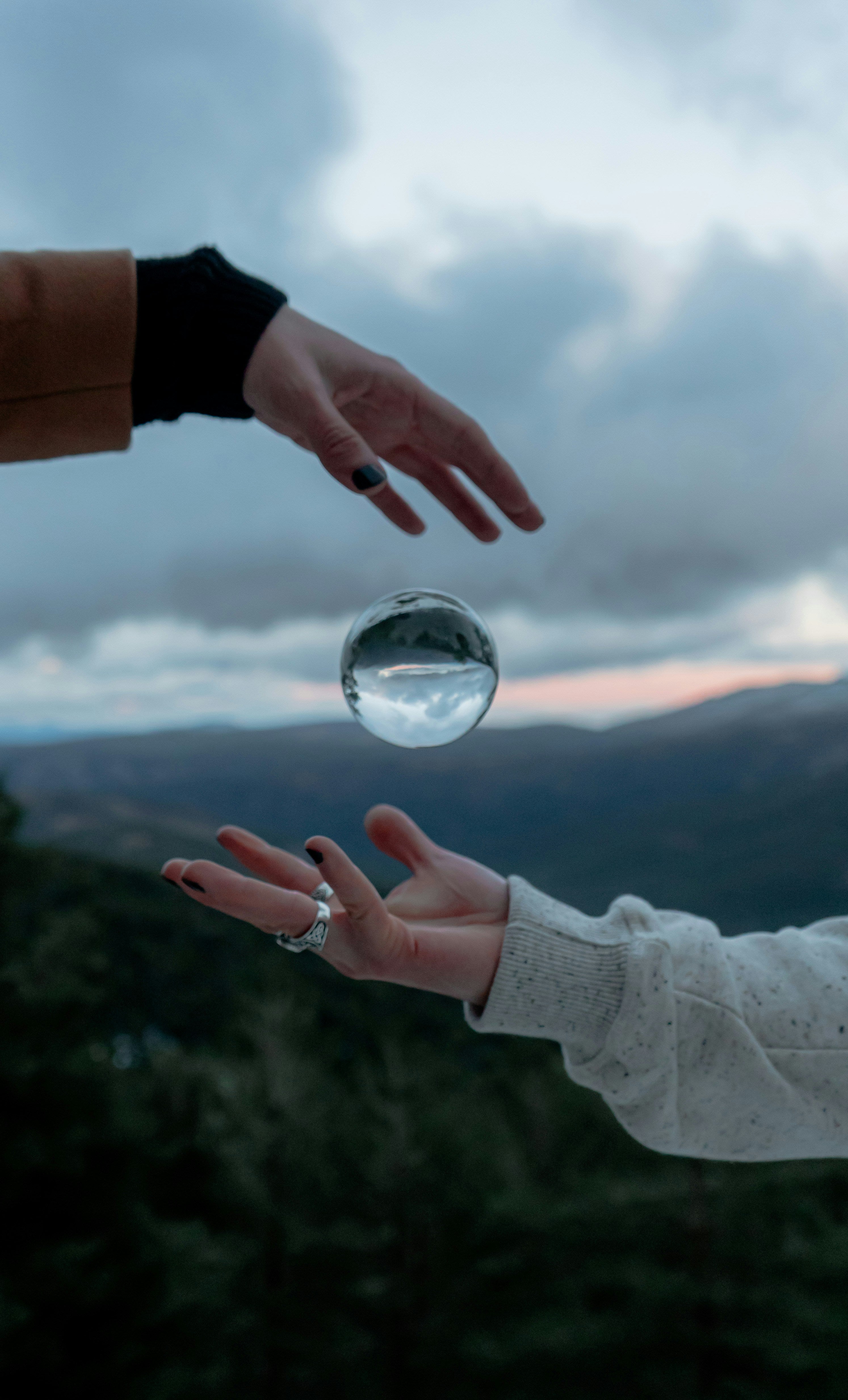 Two hands reaching towards a crystal ball with a mountainous landscape in the background