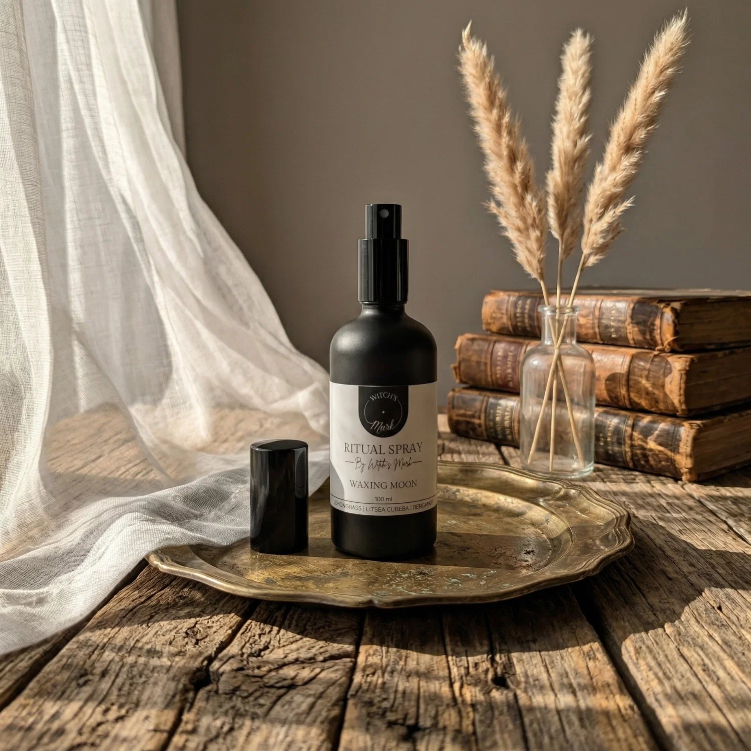 The matte black bottle of Waxing Moon ritual spray with its white label elegantly displayed on a vintage brass tray atop a rustic wooden table bathed in sunlight. This sacred elixir is perfect for misting over your altar to align with building lunar energy and manifest bold desires.