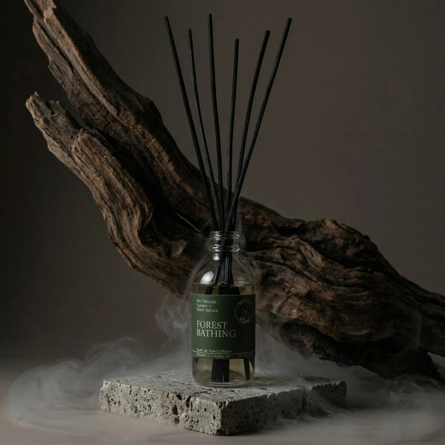 The Forest Bathing apothecary spell jar reed diffuser by Witch's Mark sitting on a stone base, enveloped in atmospheric mist with natural driftwood in the background, perfectly setting the stage for deep grounding and invoking the untamed magick of the forest floor.
