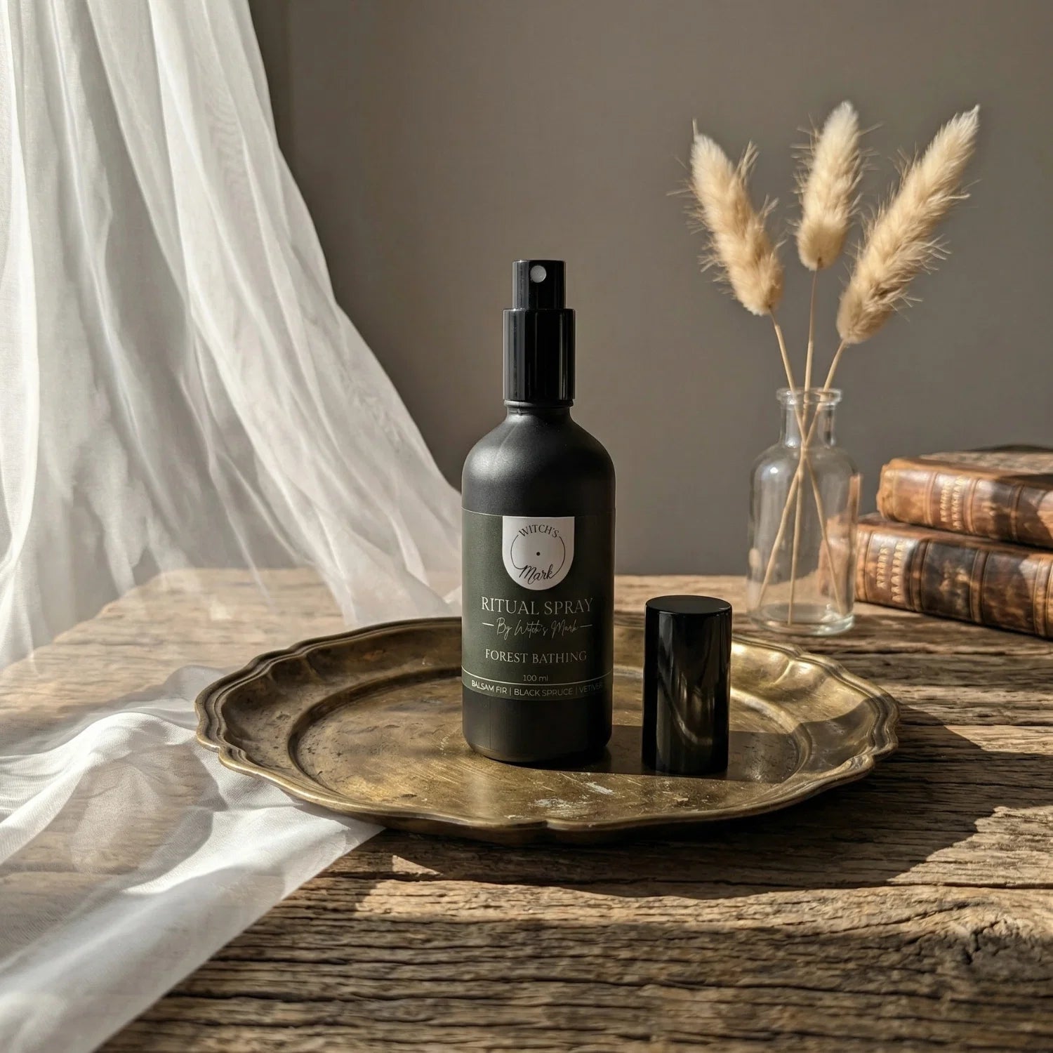 The matte black bottle of Forest Bathing ritual spray with its dark green label elegantly displayed on a vintage brass tray atop a rustic wooden table. This sacred elixir is perfect for misting over your altar to invoke stabilizing earth energies and profound energetic renewal.