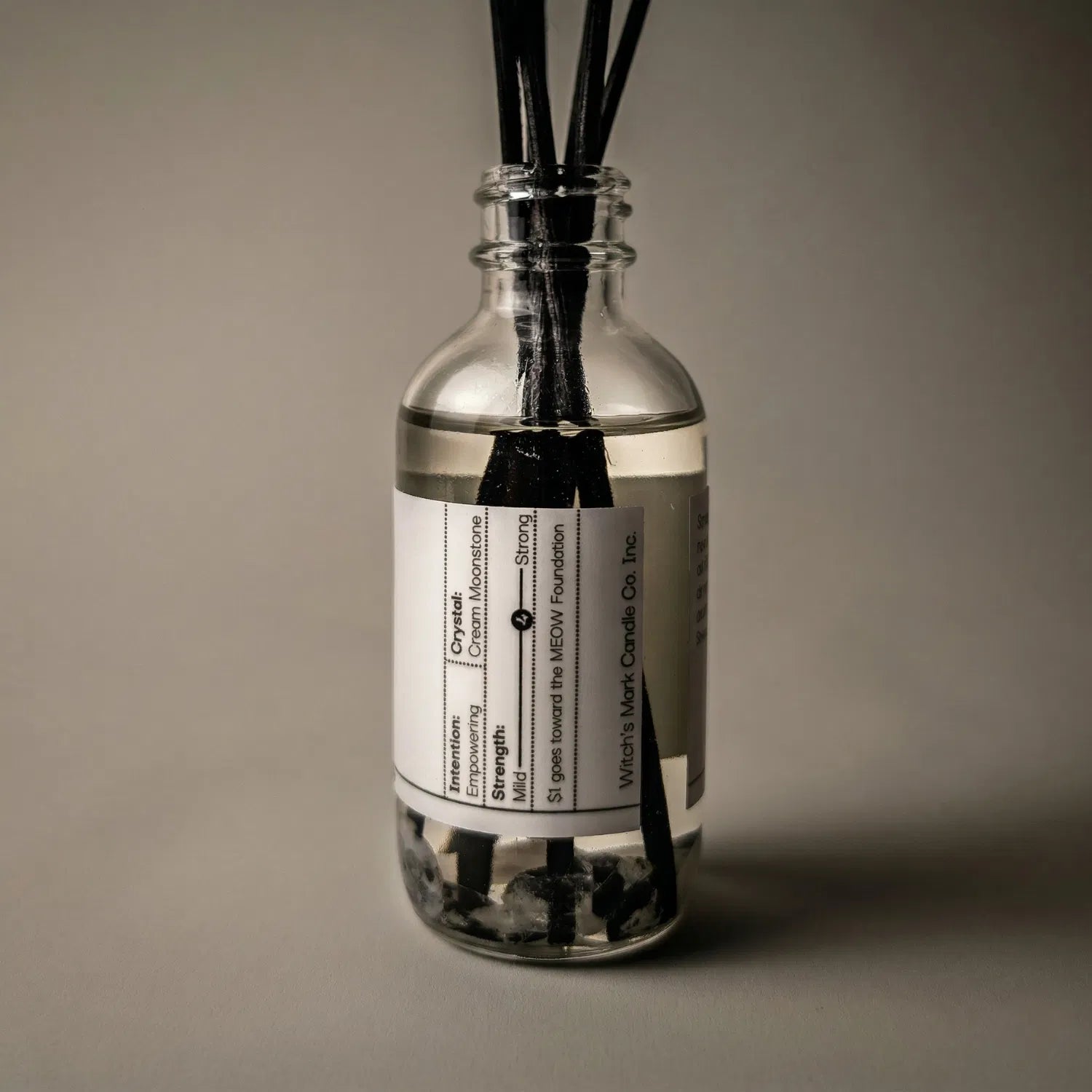 A warmly lit close-up of the Full Moon spell jar reed diffuser, revealing the potent cream moonstone crystals submerged at the bottom of the clear botanical oil, crafted to invoke emotional balance and ultimate self-empowerment.