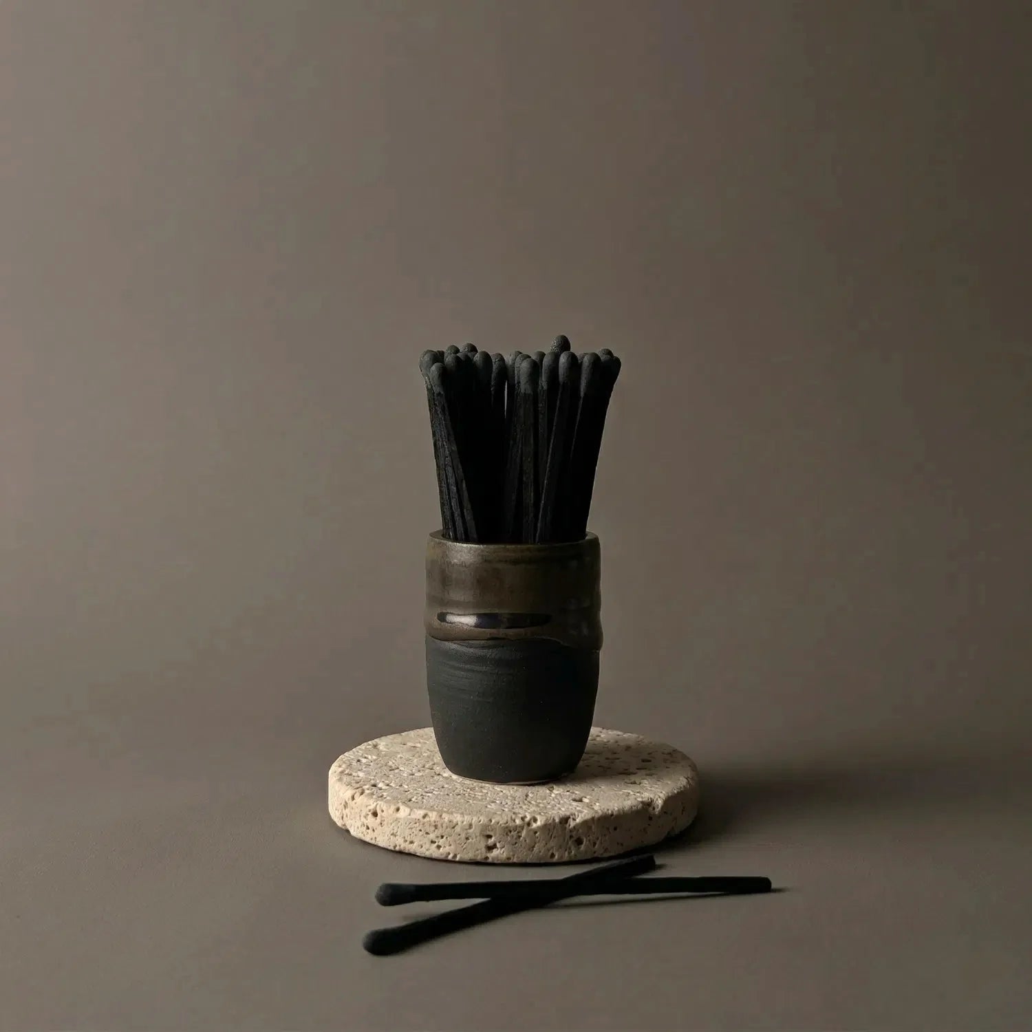 A beautifully hand-crafted ceramic cauldron match holder filled with black-on-black matches, sitting on a textured stone coaster. The unique matte black cauldron features a twilight glaze rim, creating the perfect natural lighting tool for magick candles on your witchcraft altar.