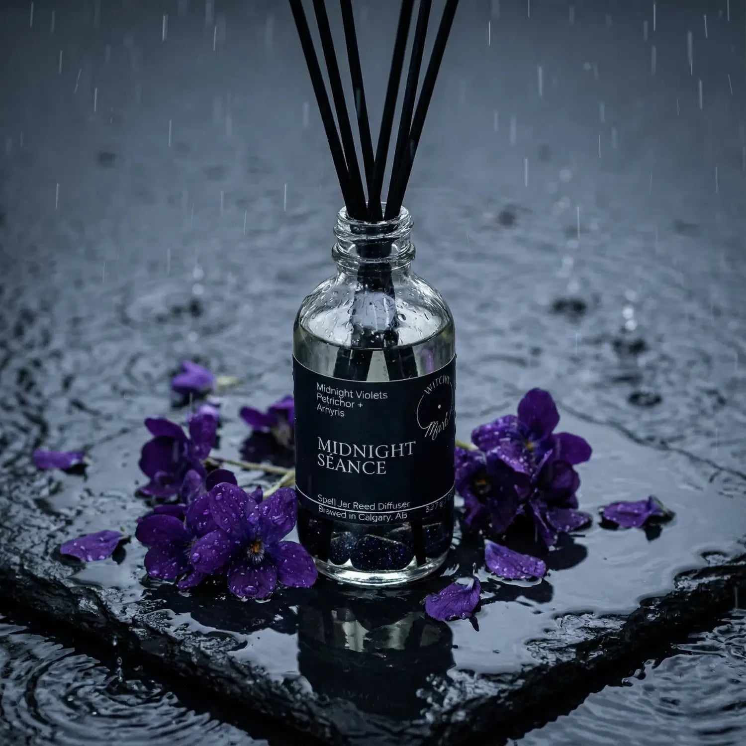 The Midnight Séance spell jar reed diffuser by Witch's Mark showcased against a dark, rain-splattered slate background representing earthy petrichor, surrounded by its core illuminating botanical ingredient of fresh purple midnight violets.