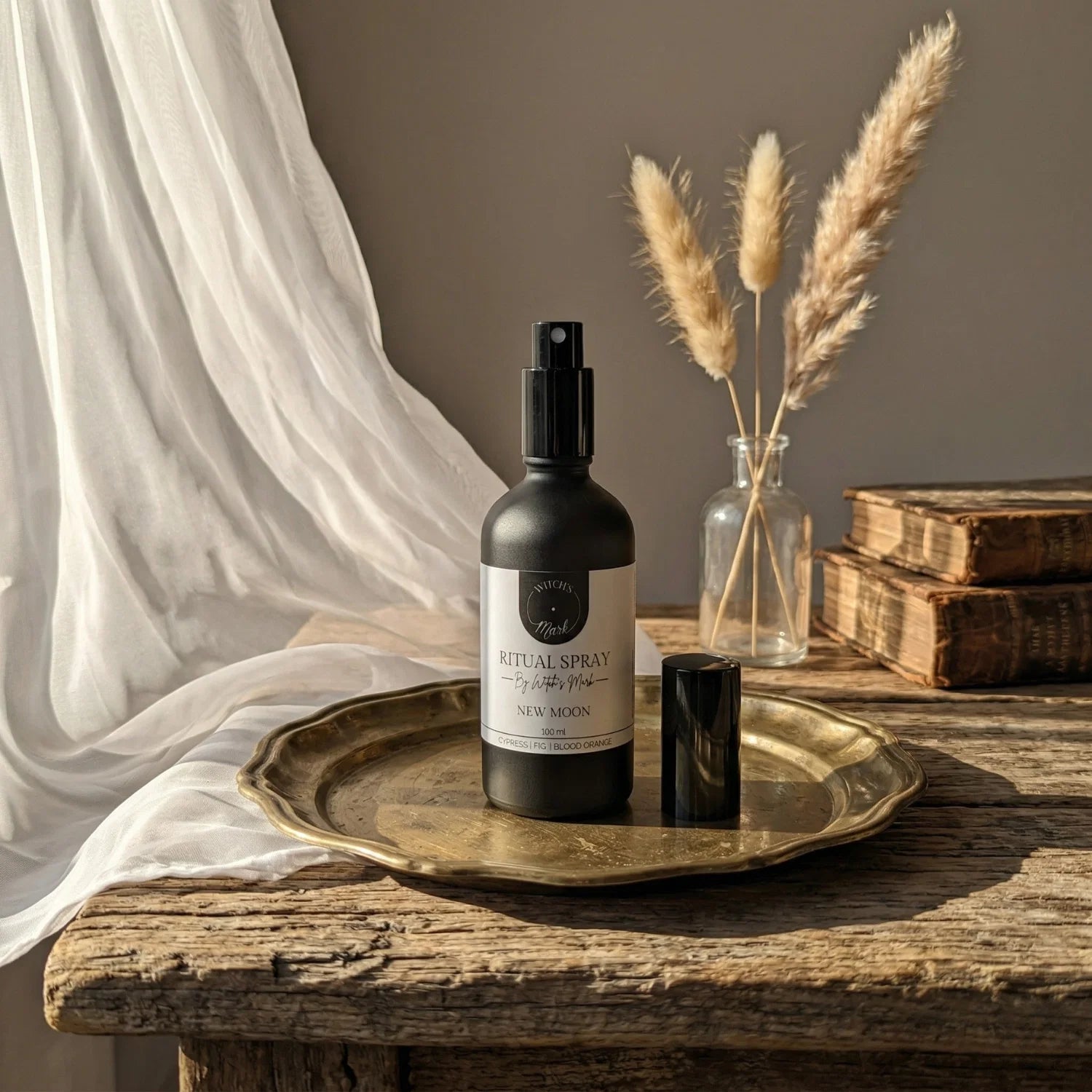 The matte black bottle of New Moon ritual spray with its white label elegantly displayed on a vintage brass tray atop a rustic wooden table bathed in soft light. This sacred elixir is perfect for misting over your altar to sweep away mental fog and prepare your spirit for powerful manifestation.