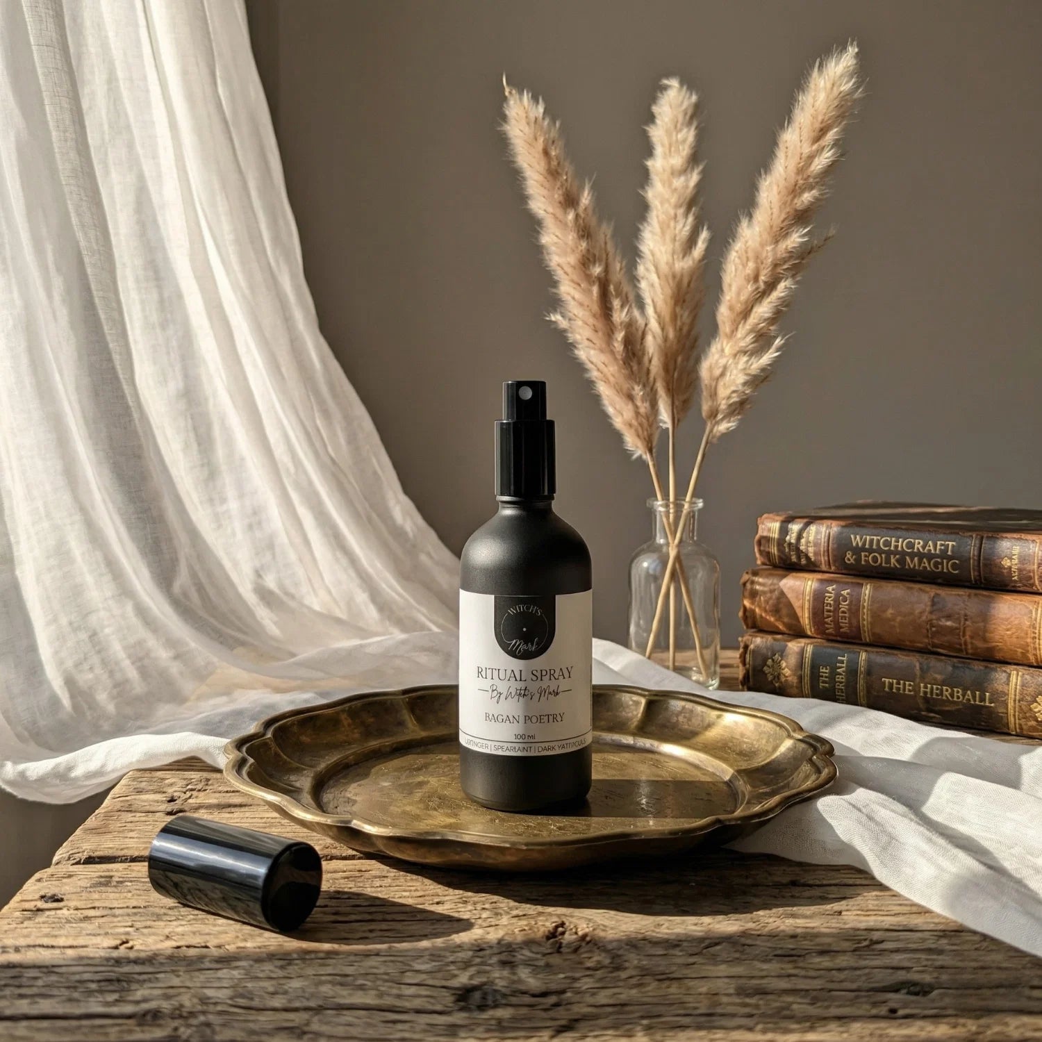 The matte black bottle of Pagan Poetry ritual spray with its white label elegantly displayed on a vintage brass tray atop a rustic wooden table, perfect for misting over your altar to induce deep relaxation and elevate your spiritual craft.