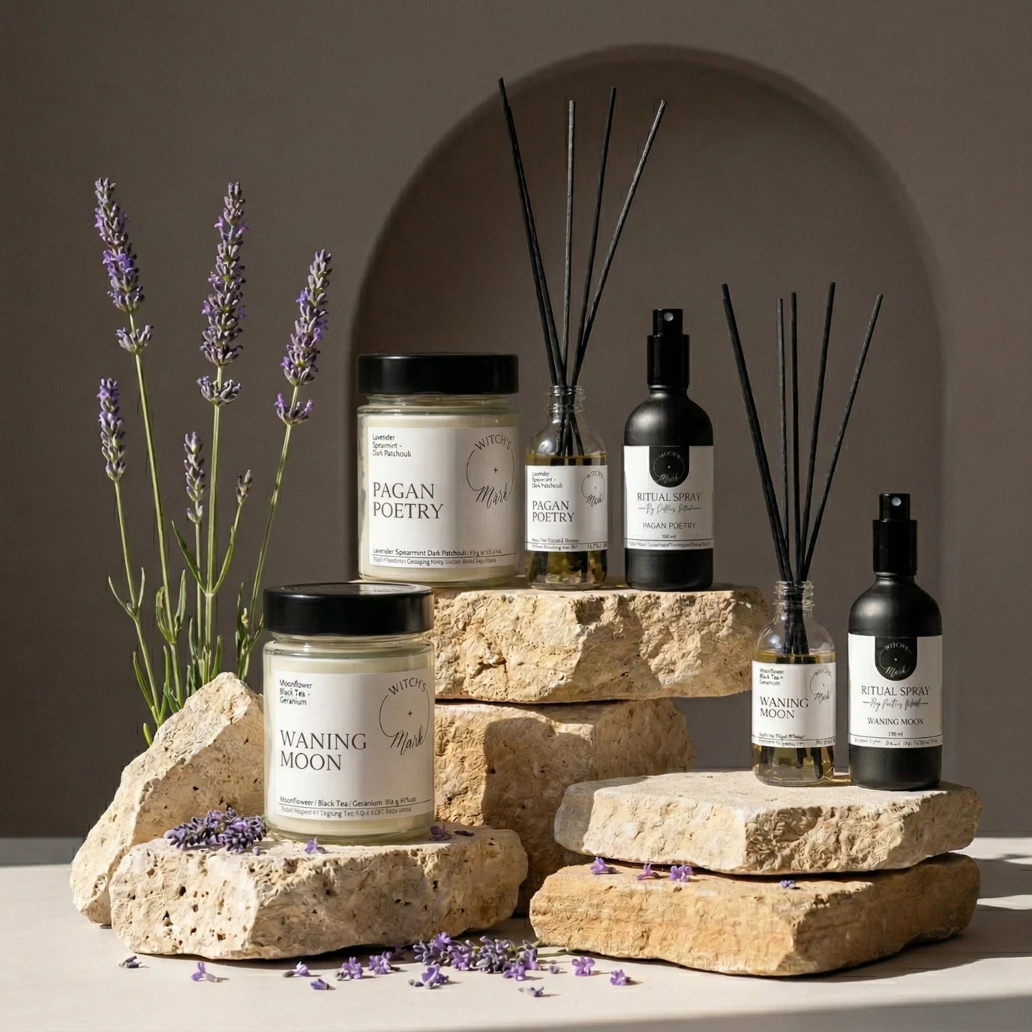 The complete Release and Restore Ritual Bundle by Witch's Mark, featuring Pagan Poetry and Waning Moon crystal candles, spell jar reed diffusers, and ritual sprays beautifully arranged on textured stones with fresh lavender.