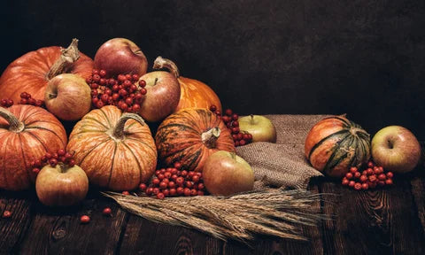 A table is decorated with an autumn spread that includes small pumpkins, gourds and wheat grass