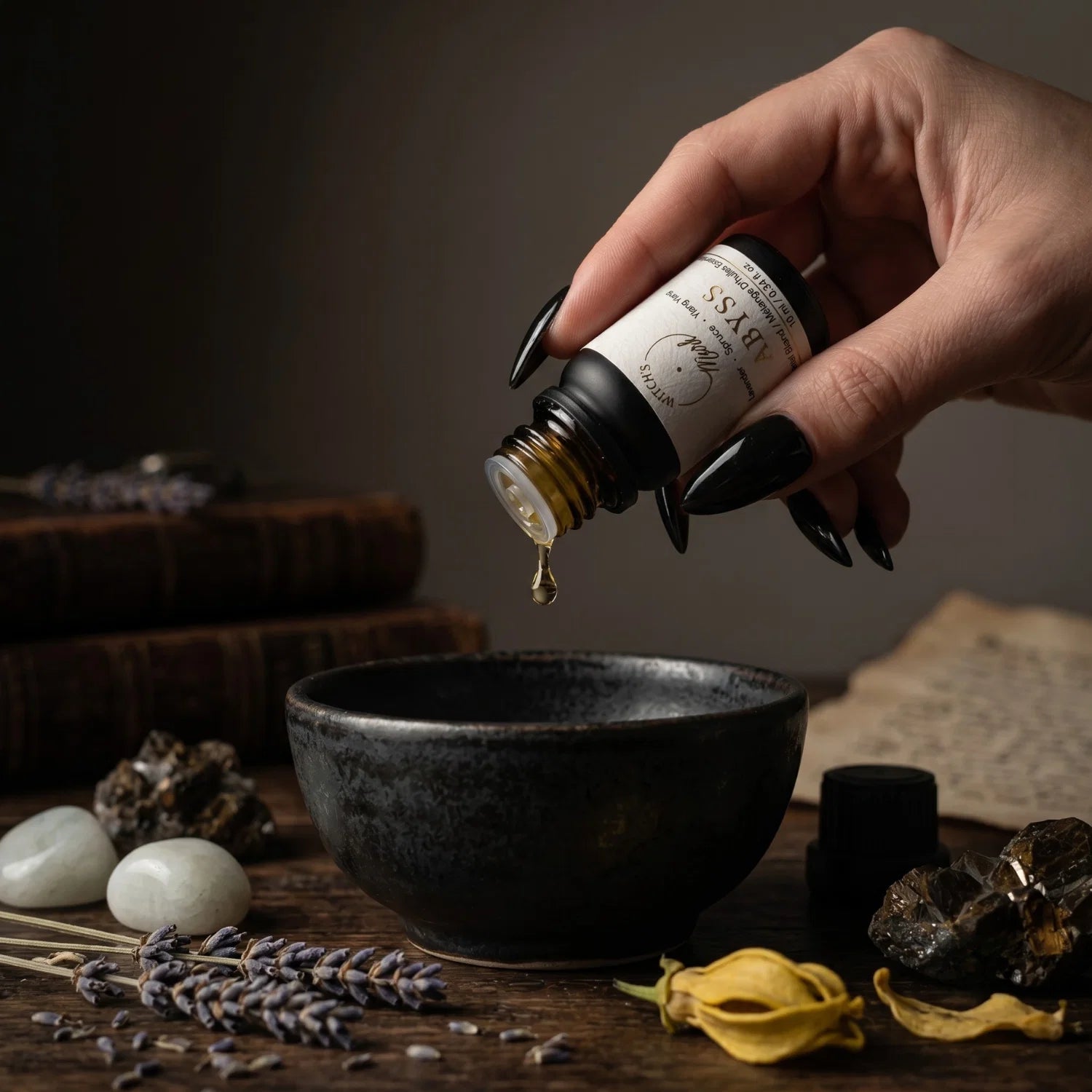 Hand pouring oil from an Abyss essential oil blend bottle into a black bowl with dried lavender, ylang ylang and a dark background.