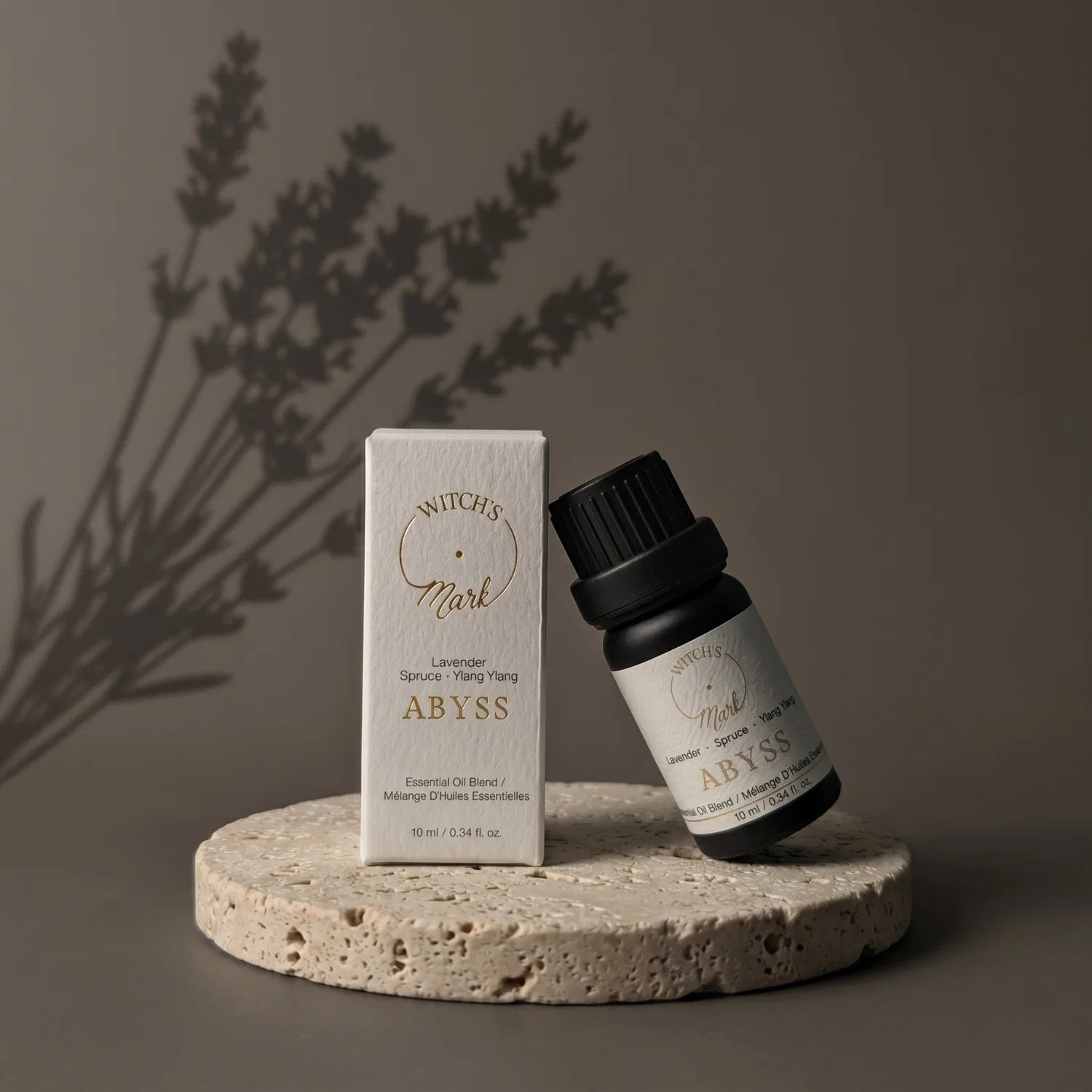 ABYSS essential oil bottle and packaging on a stone surface with a shadow of a lavender sprig in the background
