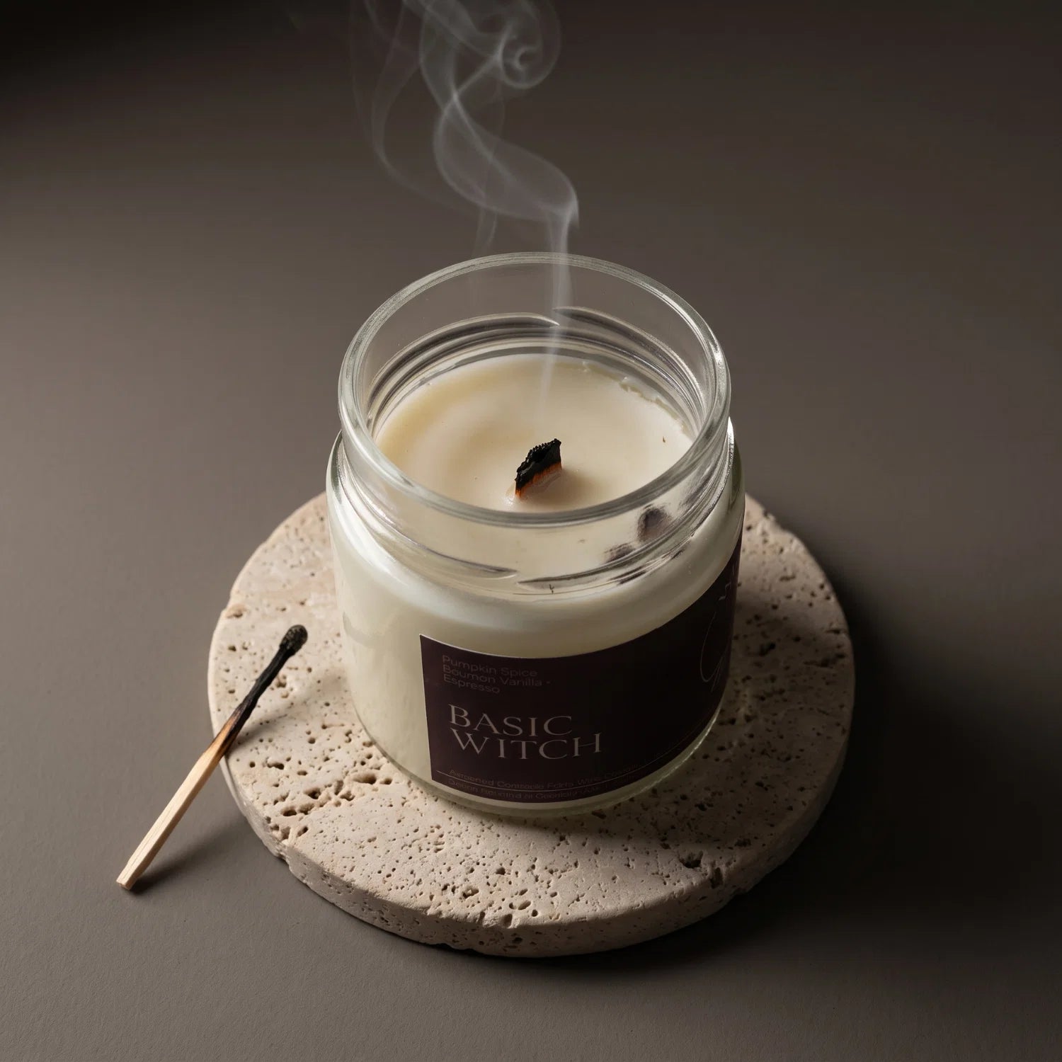 A top view of a Witch's Mark Basic Witch candle with it's wick recently extinguished. The candle rests on a porous stone coaster with a match next to it.
