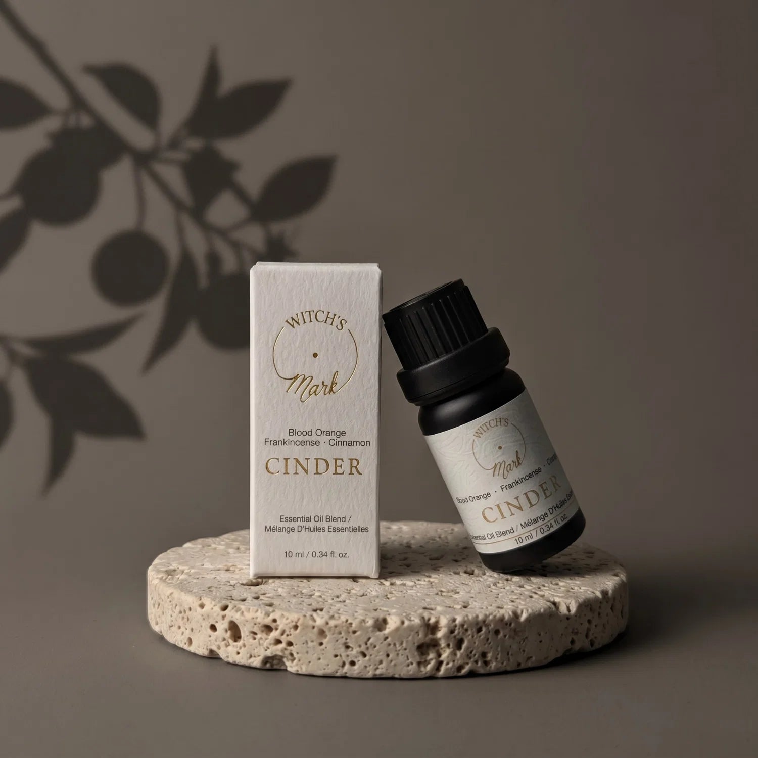 Cinder essential oil bottle leaning against box on a porous coaster. In the background is a shadow of a blood orange branch.