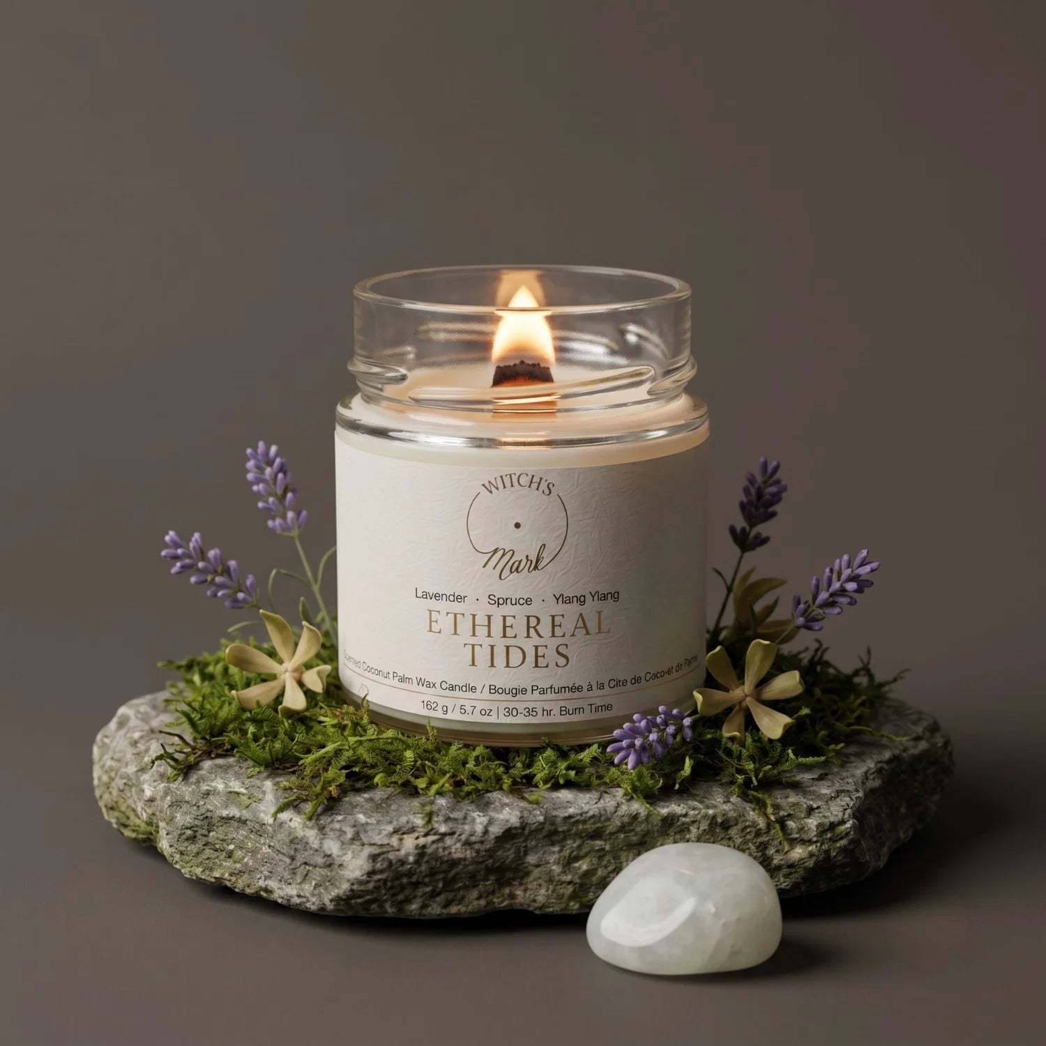 Candle in a glass jar labeled 'Ethereal Tides' on a stone surface with lavender and moss.