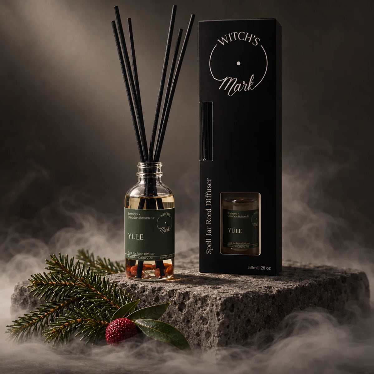 A Witch's Mark 'Yule' spell jar reed diffuser set, featuring a glass bottle with black reeds, a dark green label, and its black packaging box, styled on a stone pedestal with mist, balsam branches, and a red bayberry.
