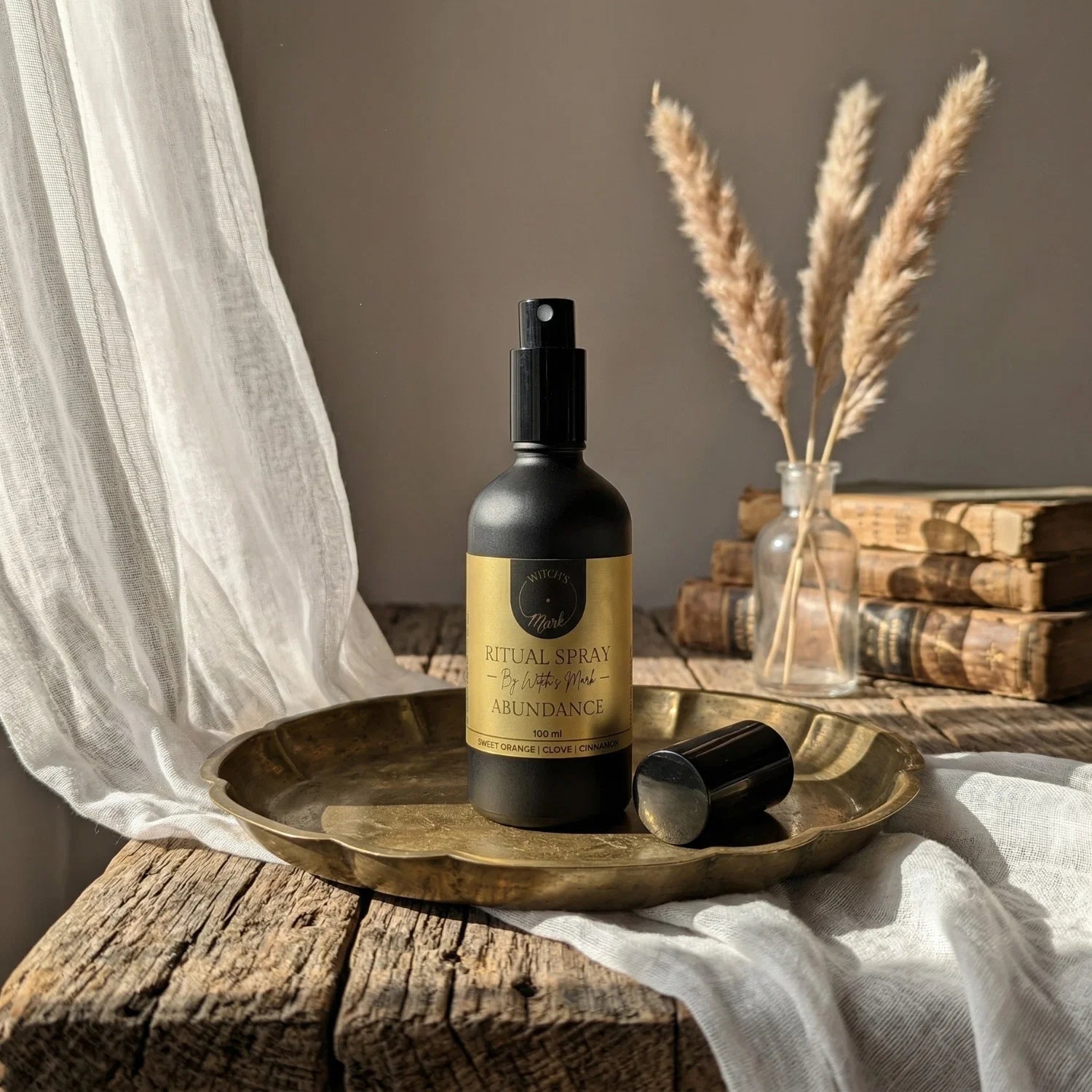 The matte black bottle of Abundance ritual spray with its radiant gold label elegantly displayed on a vintage brass tray atop a rustic wooden table bathed in sunlight. This sacred elixir is perfect for misting over your altar or threshold to attract golden luck and endless opportunity.