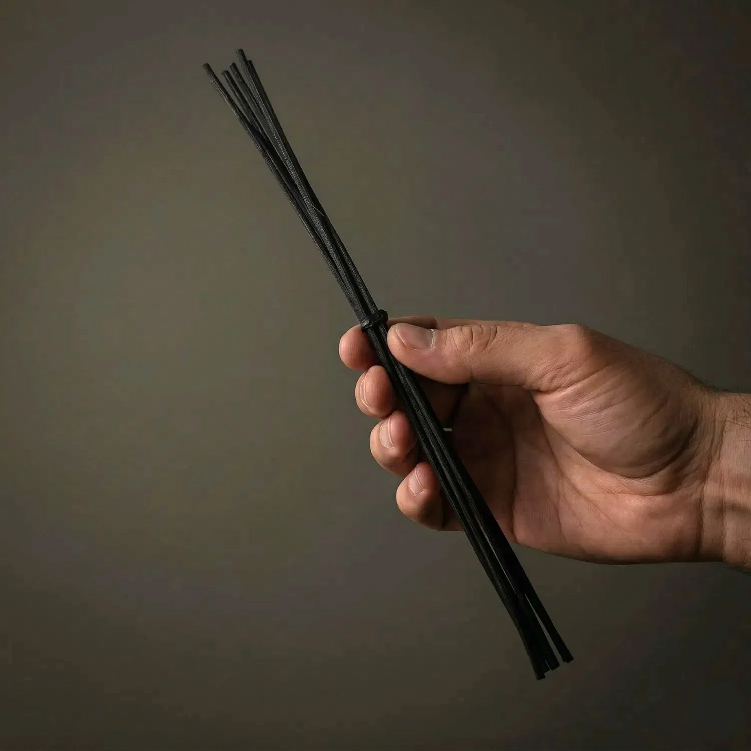 A hand holding a bundled 6-pack of high-quality black rattan replacement reeds against a dark, moody background. These essential diffuser sticks are designed to efficiently absorb and disperse your favorite Witch's Mark room fragrances.