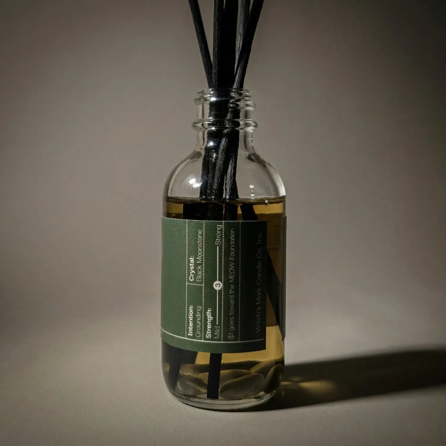 A warmly lit close-up of the Forest Bathing spell jar reed diffuser, revealing the stabilizing black moonstone crystals submerged at the bottom of the golden botanical oil, crafted to transform your sacred sanctuary into a haven of profound peace.