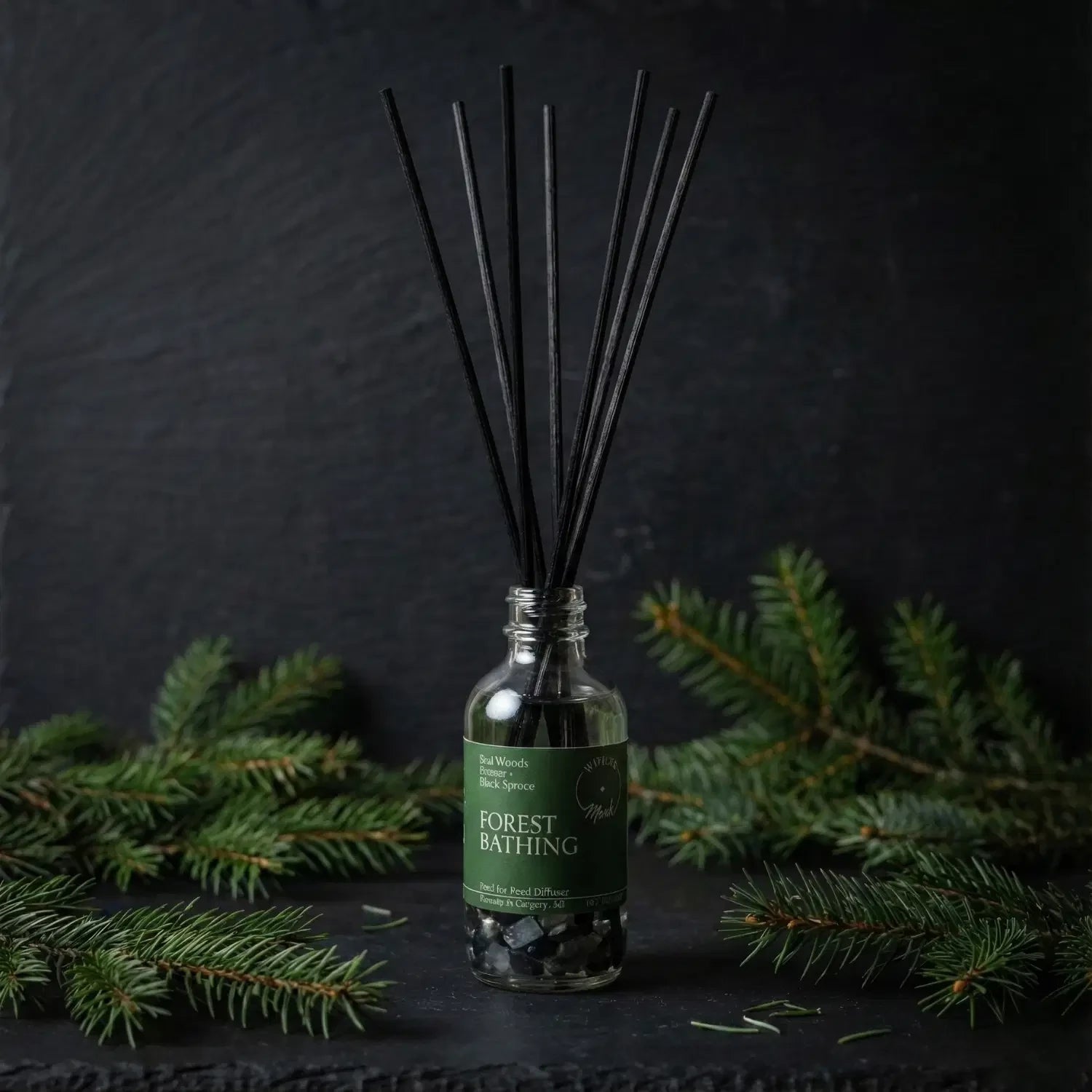 The Forest Bathing spell jar reed diffuser by Witch's Mark showcased against a dark slate background, surrounded by its core grounding botanical ingredients of fresh, aromatic black spruce and balsam branches.