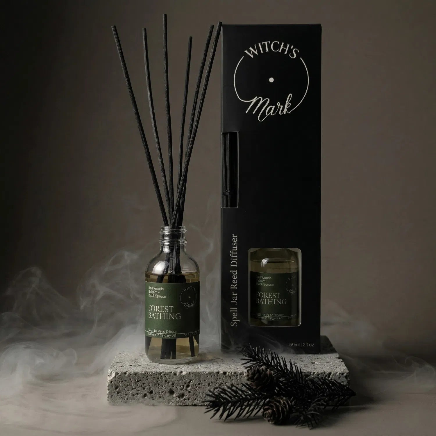 A Forest Bathing spell jar reed diffuser by Witch's Mark displayed with its dark packaging and fresh black spruce sprigs, offering continuous flame-free grounding aromatherapy amidst a misty atmosphere.