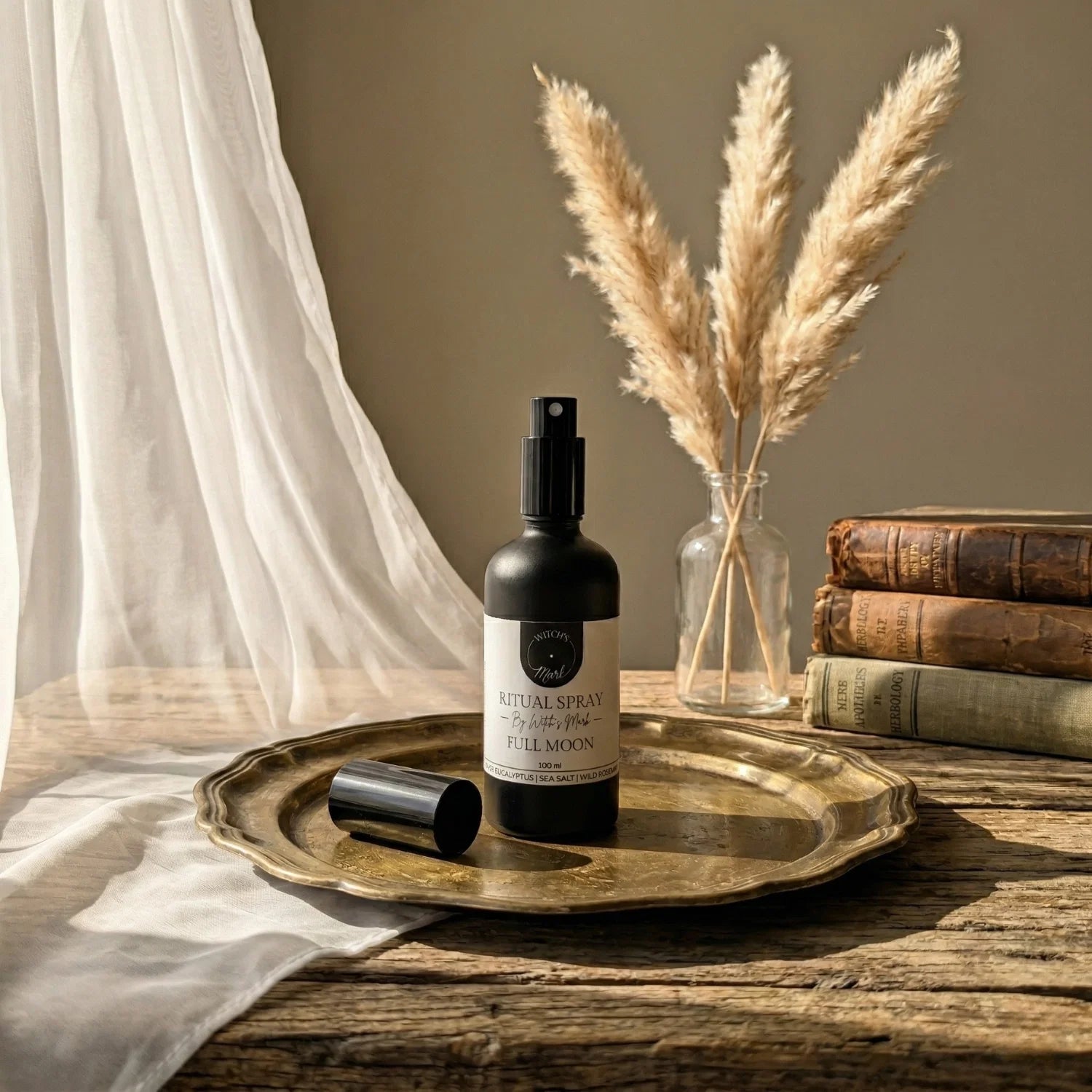 The matte black bottle of Full Moon ritual spray with its white label elegantly displayed on a vintage brass tray atop a rustic wooden table bathed in soft light. This sacred elixir is perfect for misting over your altar to empower divination, amplify your magick, and draw down the luminous energy of the full moon.