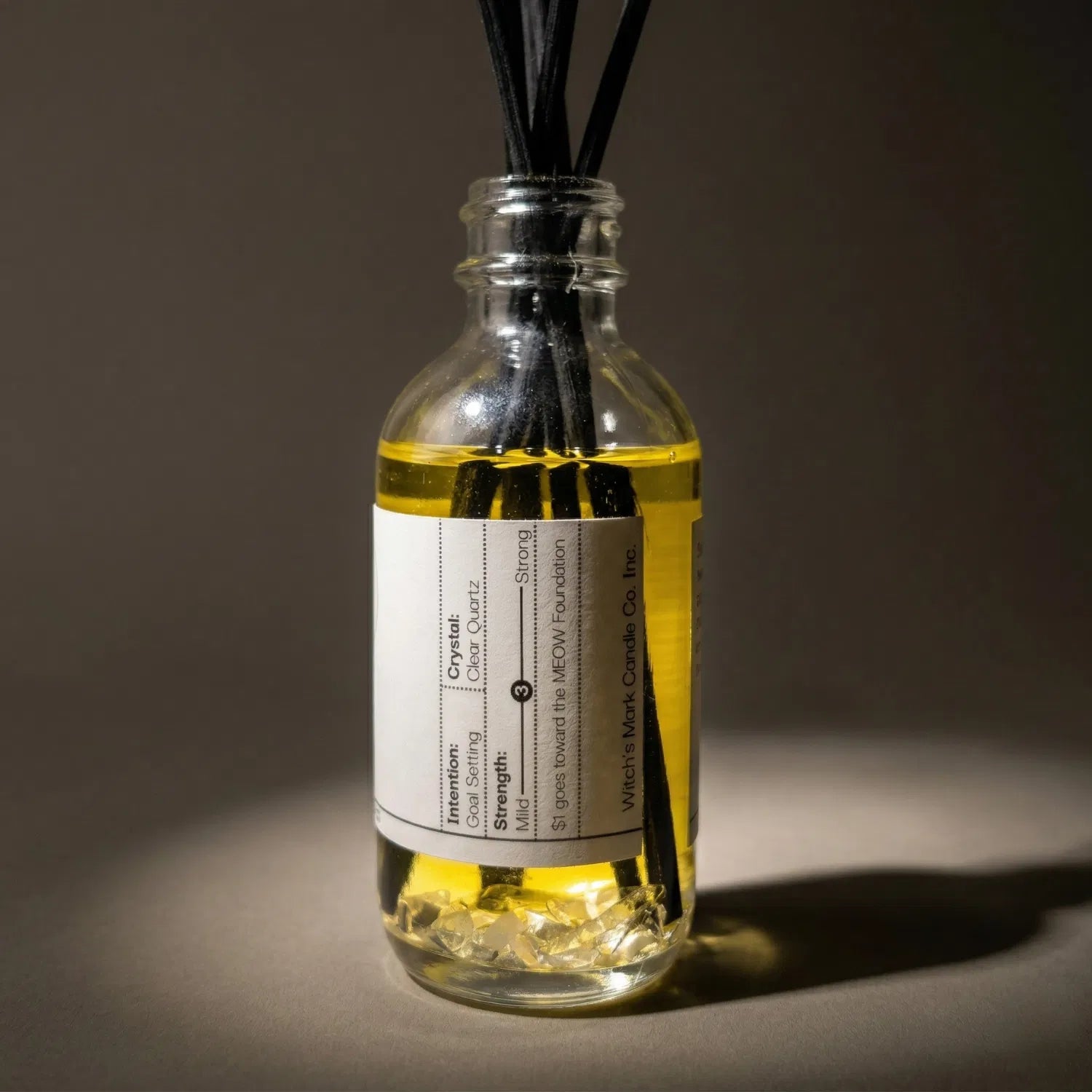 A warmly lit close-up of the New Moon spell jar reed diffuser turned slightly to reveal the amplifying clear quartz crystals submerged within the golden botanical oil, crafted to manifest your deepest desires.