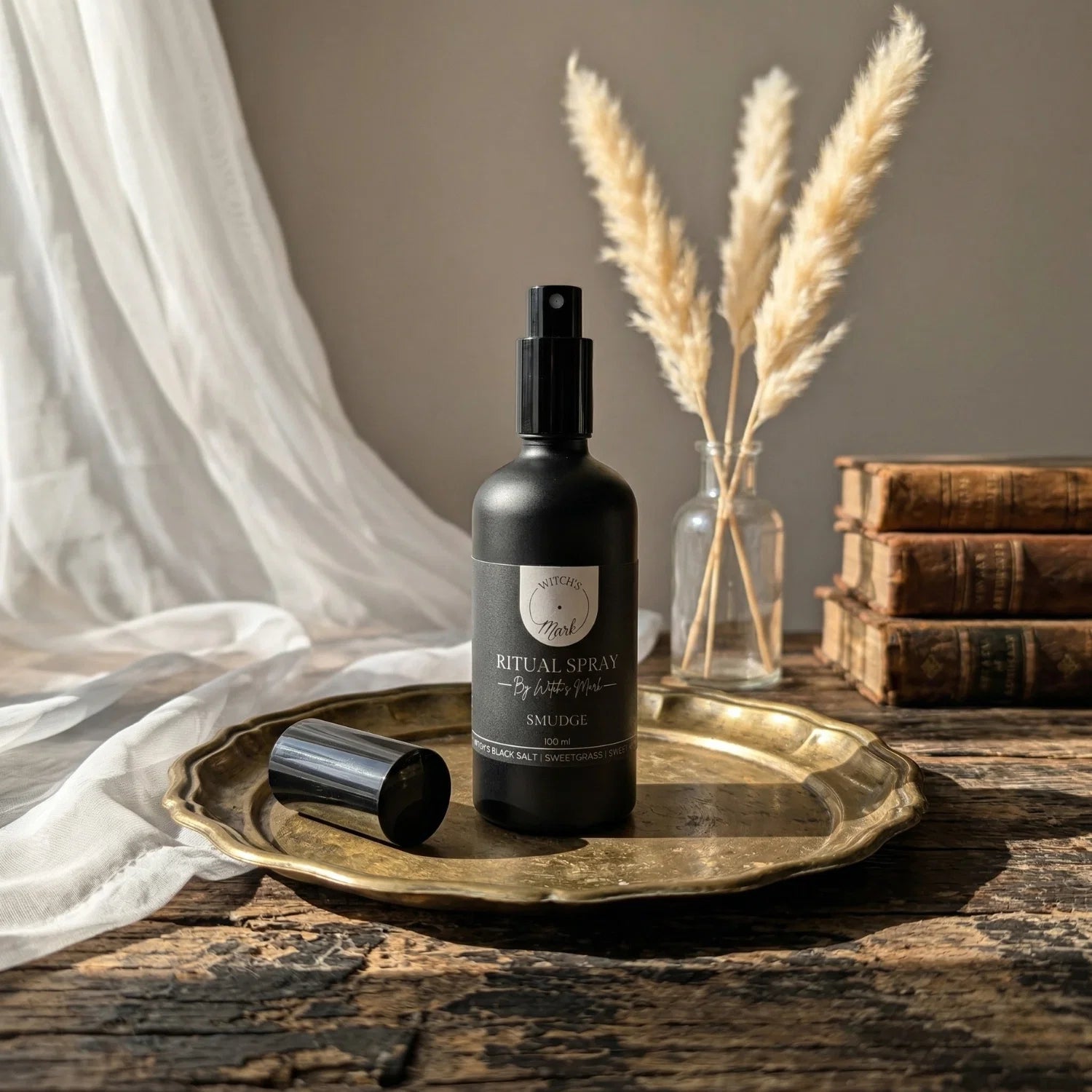 The matte black bottle of Smudge ritual spray by Witch's Mark elegantly displayed on a vintage brass tray atop a rustic wooden table, perfect for purifying your sanctuary and guarding your sacred space.