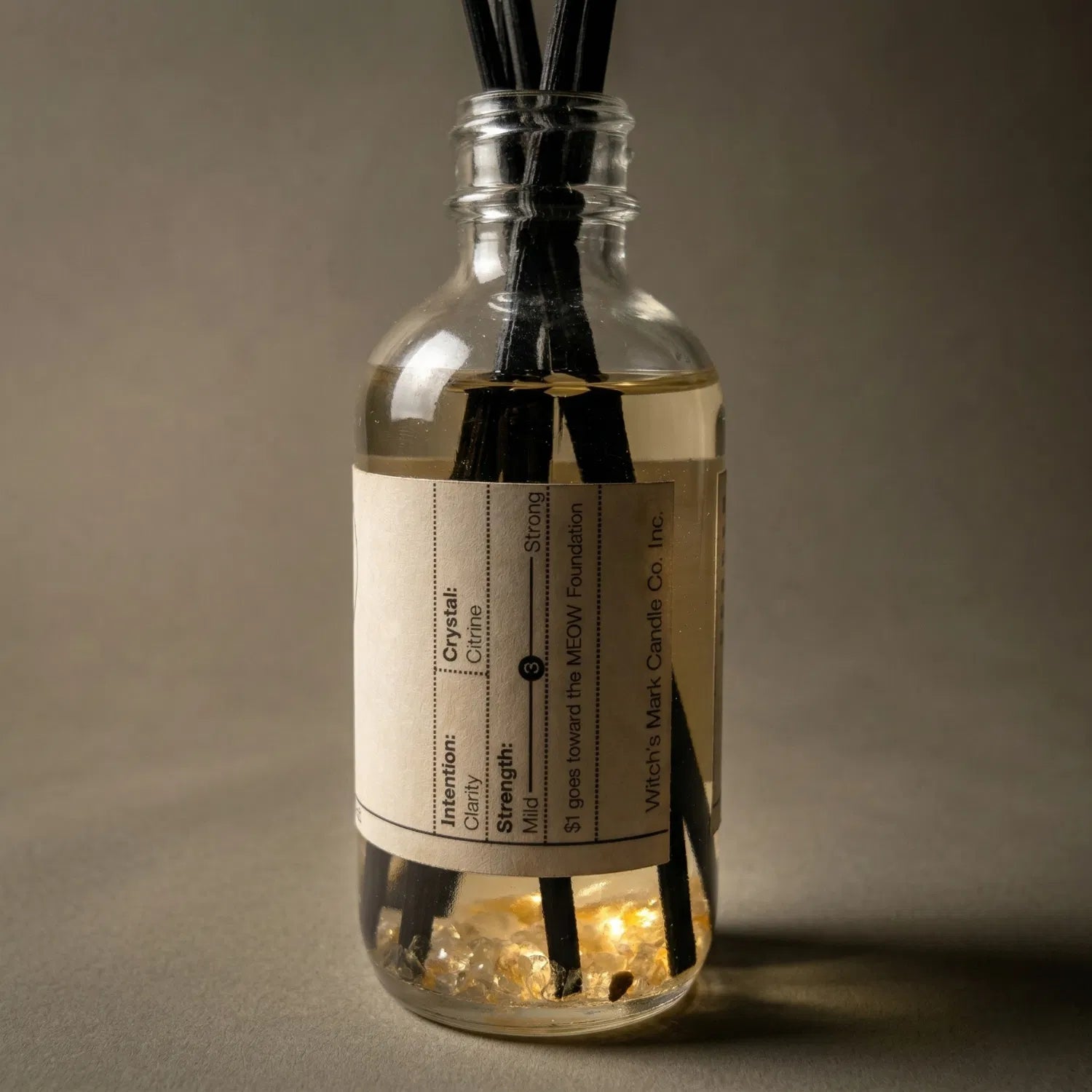 A warmly lit close-up of The Oracle spell jar reed diffuser, revealing the radiant citrine crystals submerged at the bottom of the golden botanical oil, crafted to awaken your inner fire and clear spiritual static.