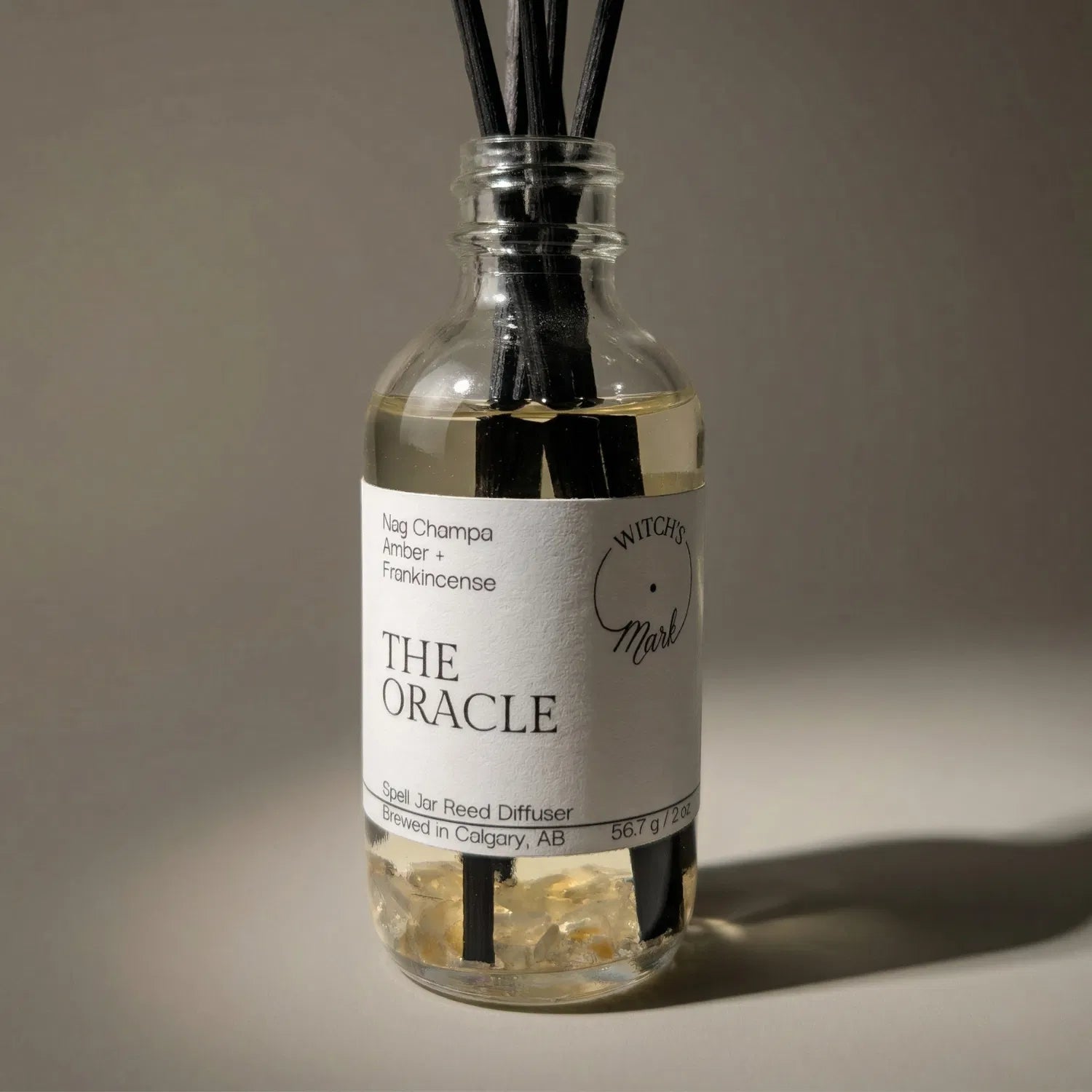 A dramatic spotlight close-up of The Oracle spell jar reed diffuser, highlighting the front label which lists its magical, hypnotic scent profile of sacred nag champa, warm resinous amber, and ancient frankincense.
