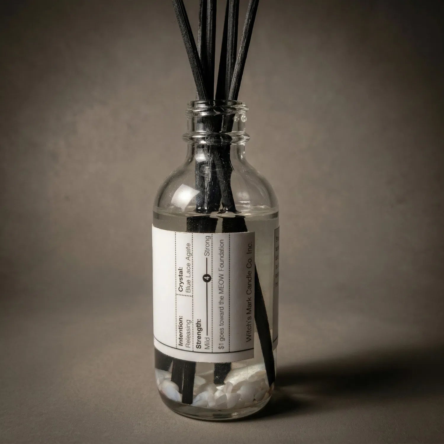 A warmly lit close-up of the Waning Moon spell jar reed diffuser, revealing the soothing blue lace agate crystals submerged at the bottom of the clear botanical oil, crafted to wrap the aura in profound calm and build quiet confidence.