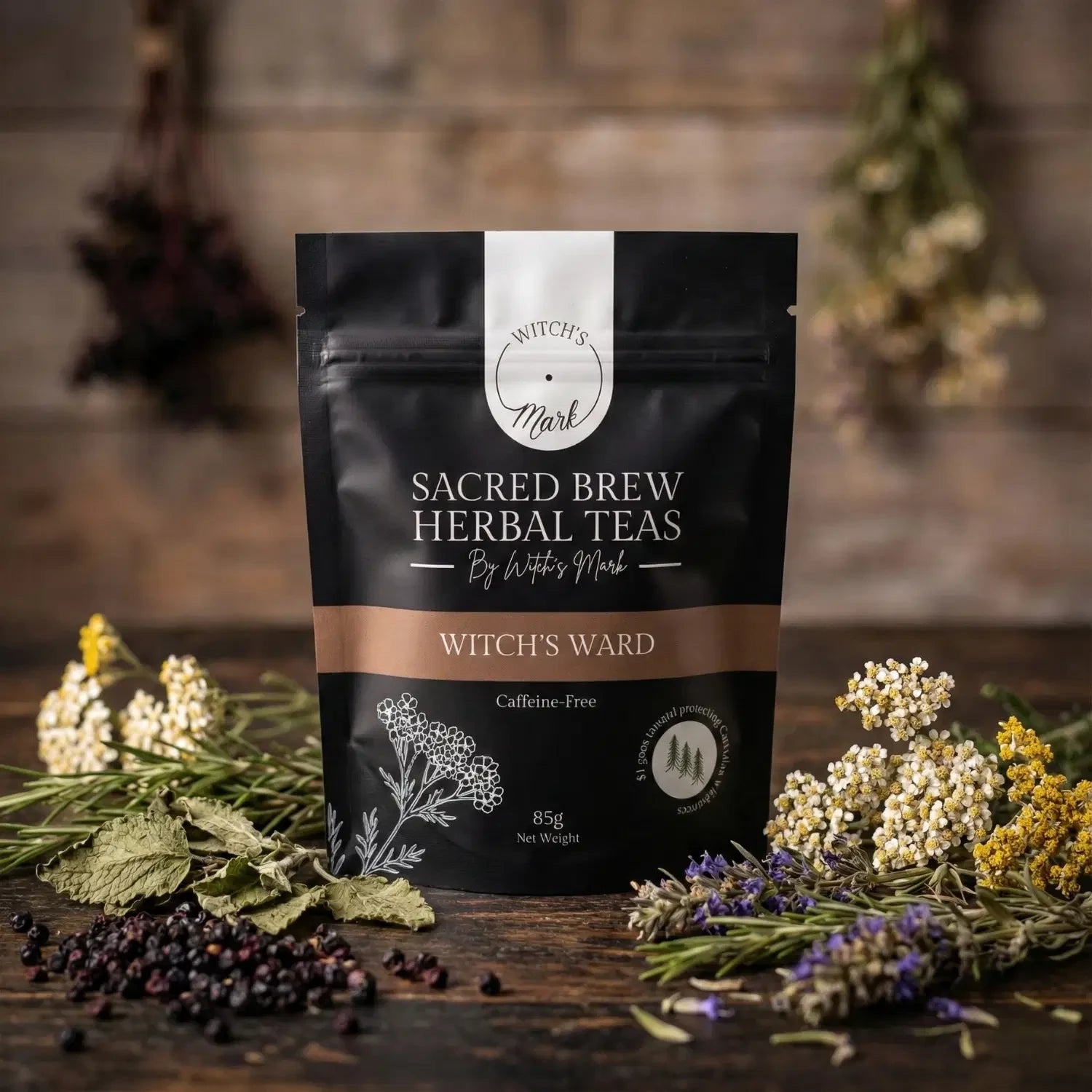 The Sacred Brew Herbal Teas Witch's Ward pouch by Witch's Mark displayed on a rustic wooden table. This caffeine-free immune support tea is surrounded by its raw, antioxidant-infused ingredients including dark dried elderberries, clusters of yarrow flowers, hyssop, lemon balm, and sprigs of fresh rosemary.